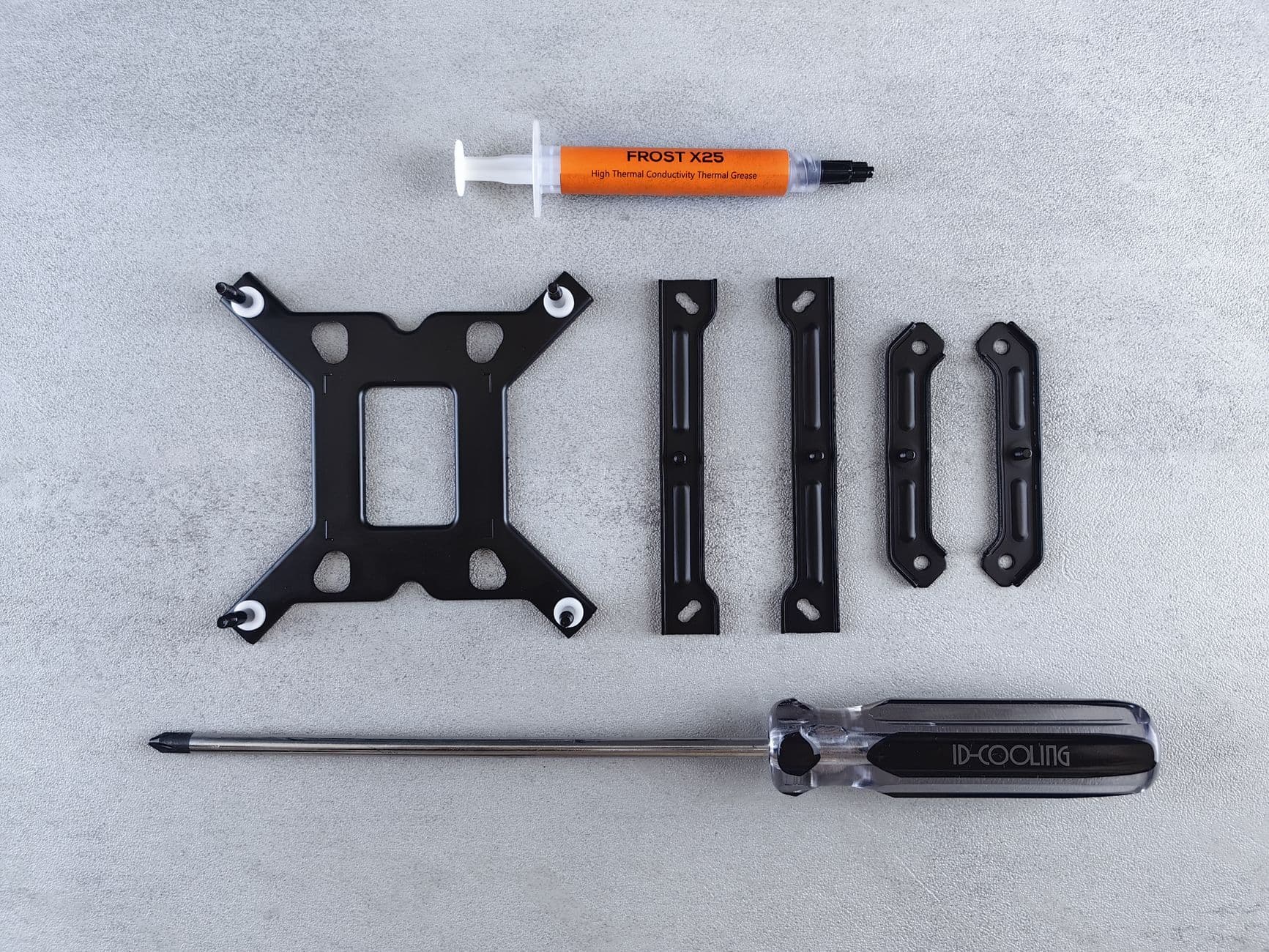 A cooler mounting kit laid out flat on concrete with brackets, thermal paste and a screwdriver