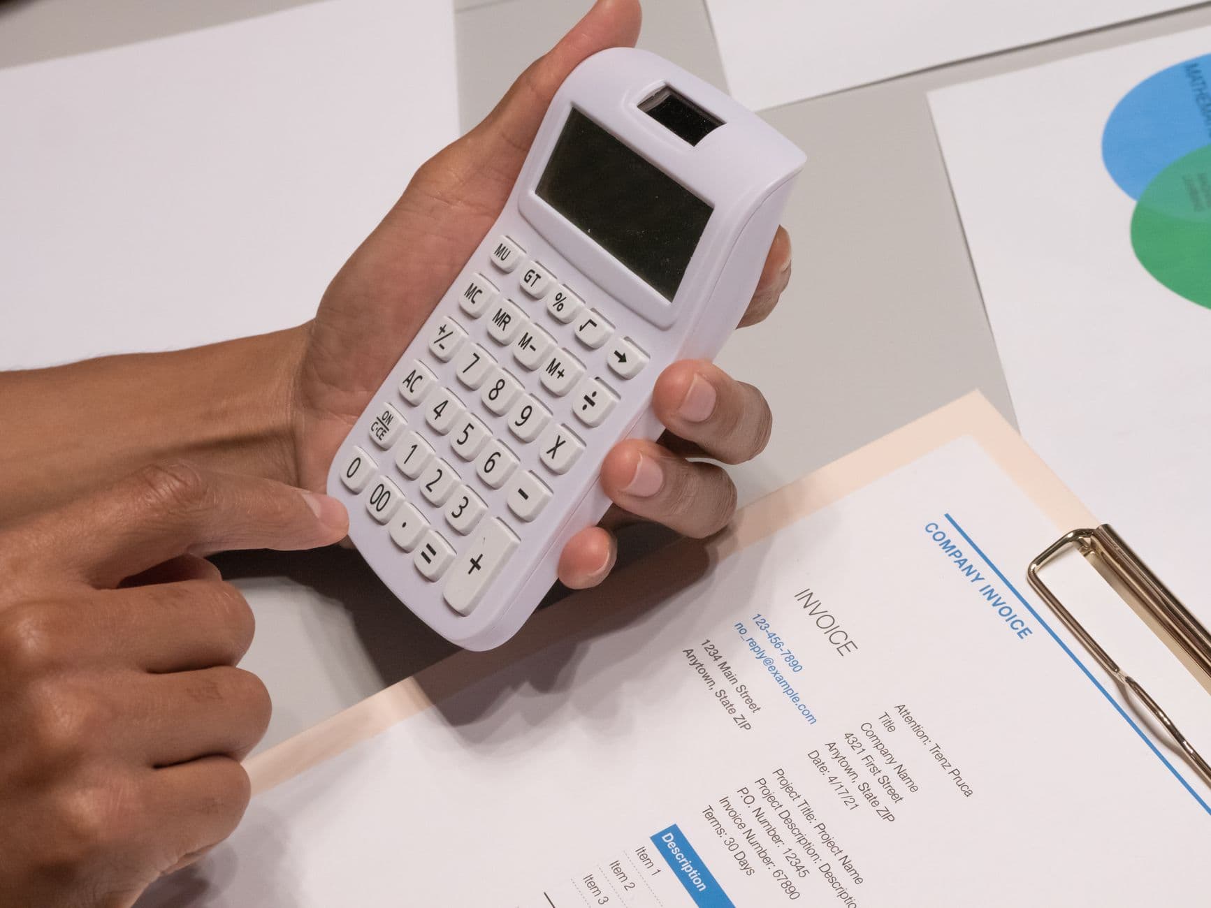 Hands working a calculator over a printed company invoice on a clipboard